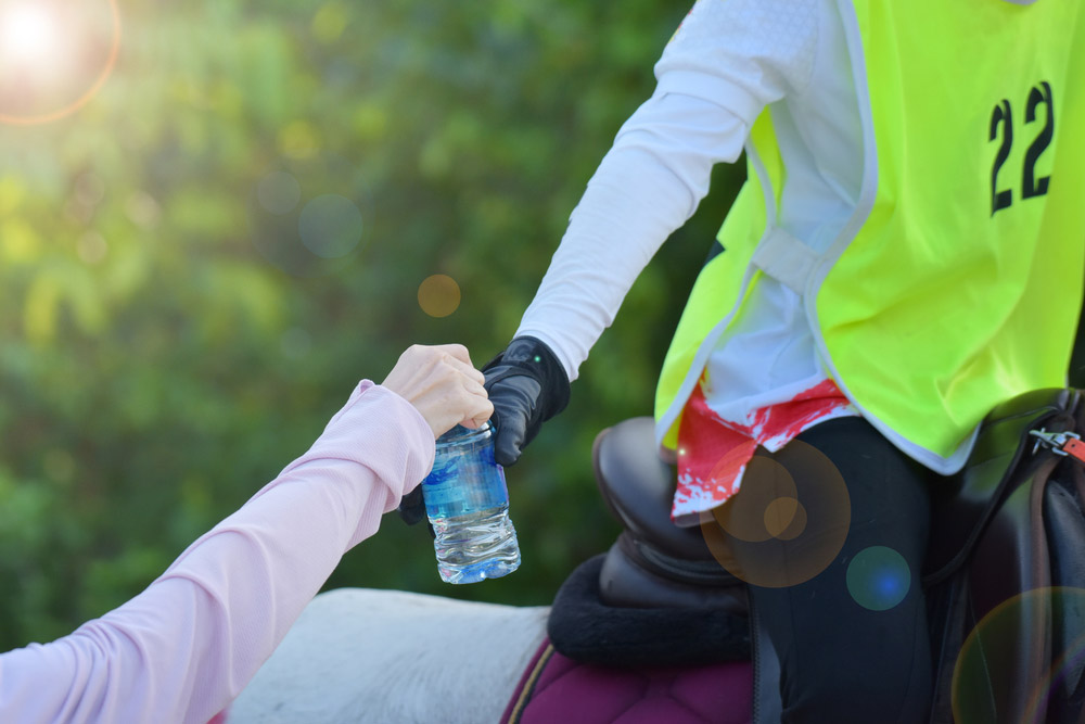 Hand a water bottle to the equestrian rider