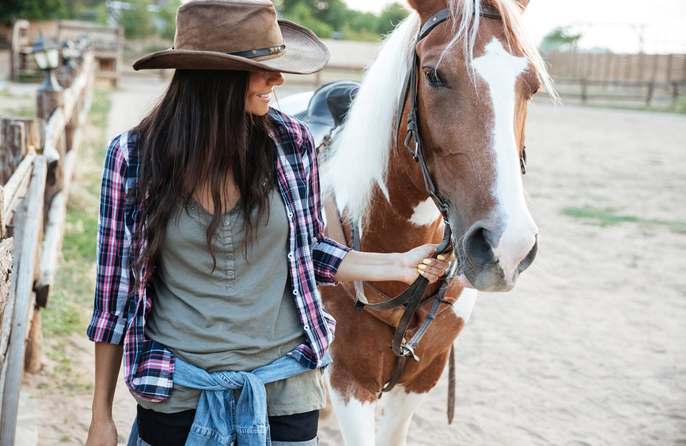Smiling lovely young woman cowgirl with her horse