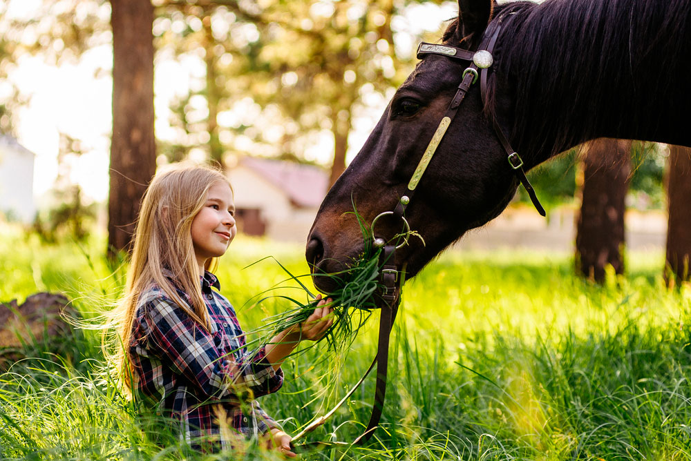 blonde girl stroking a brown horse