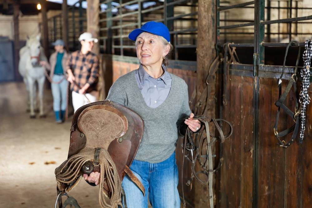 senior woman holding a horse saddle